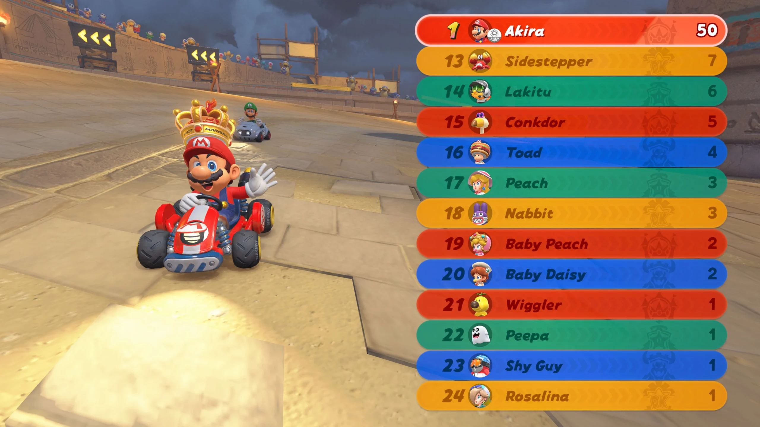 Mario in a kart leads a race on a sandy track, leaderboard shows 24 racers with Akira in first place