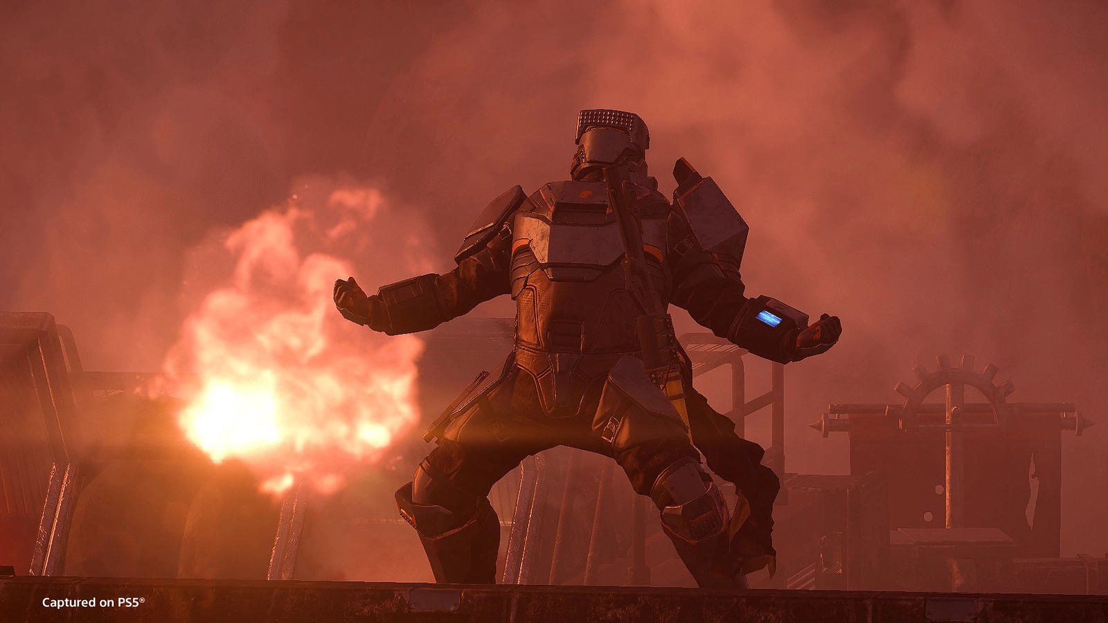 Armored soldier stands amid smoke and fire, ready for battle with powerful weaponry in Helldivers game