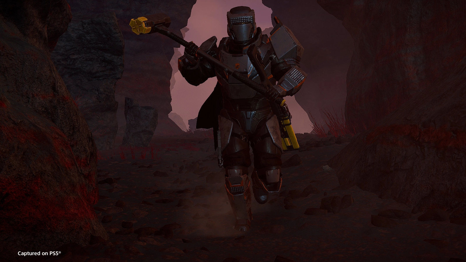 A heavily armored soldier runs through a rocky terrain, wielding a large hammer with a yellow head