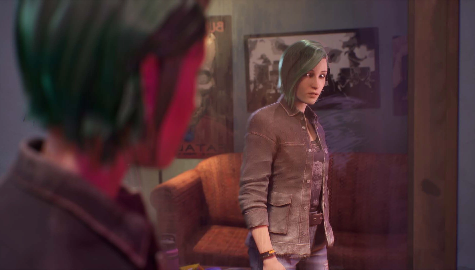 Chloe with green hair looks at her reflection in a mirror, standing in a cozy room with posters on walls