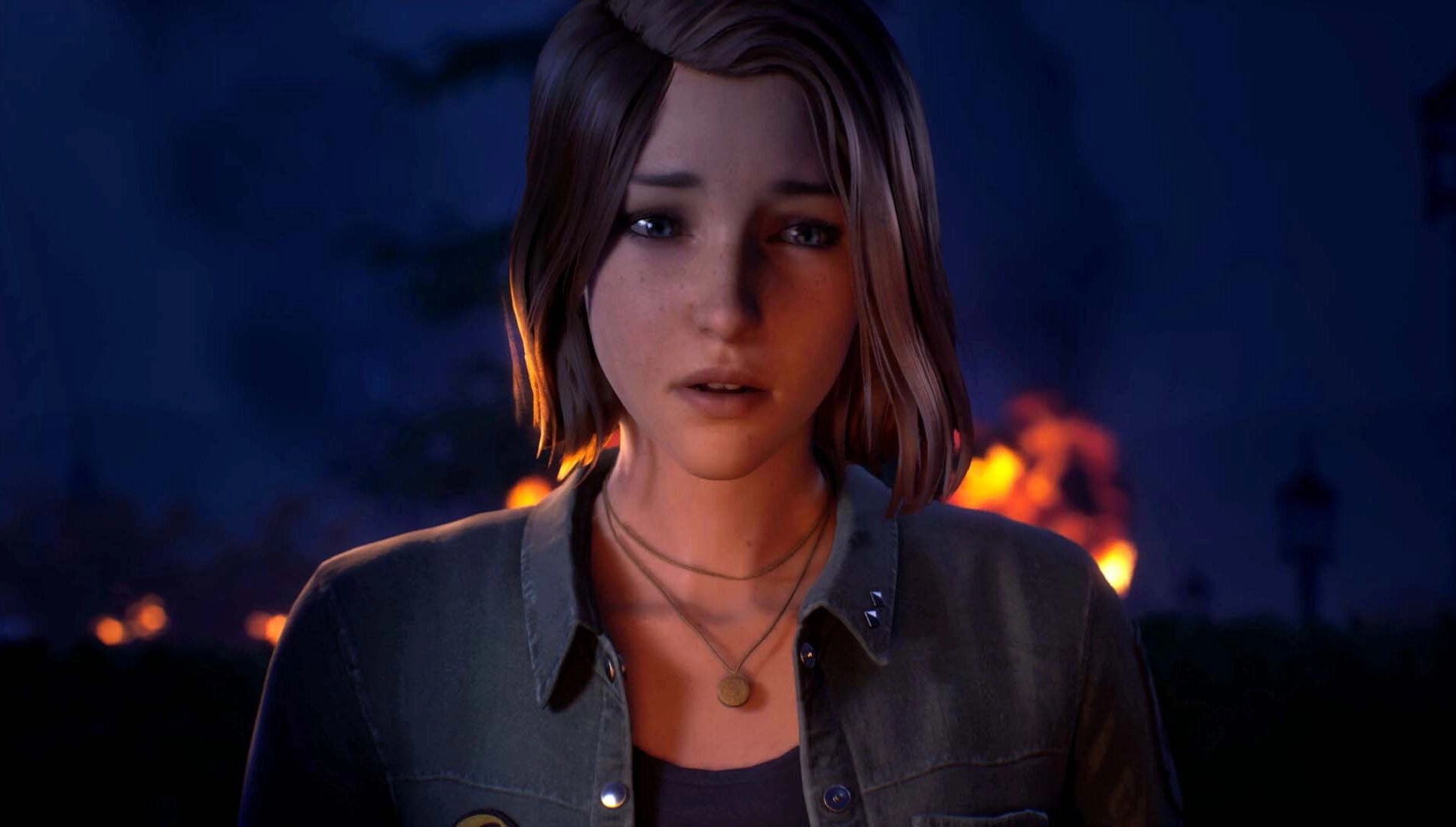 A young woman with short hair looks concerned, standing against a backdrop of distant flames at night
