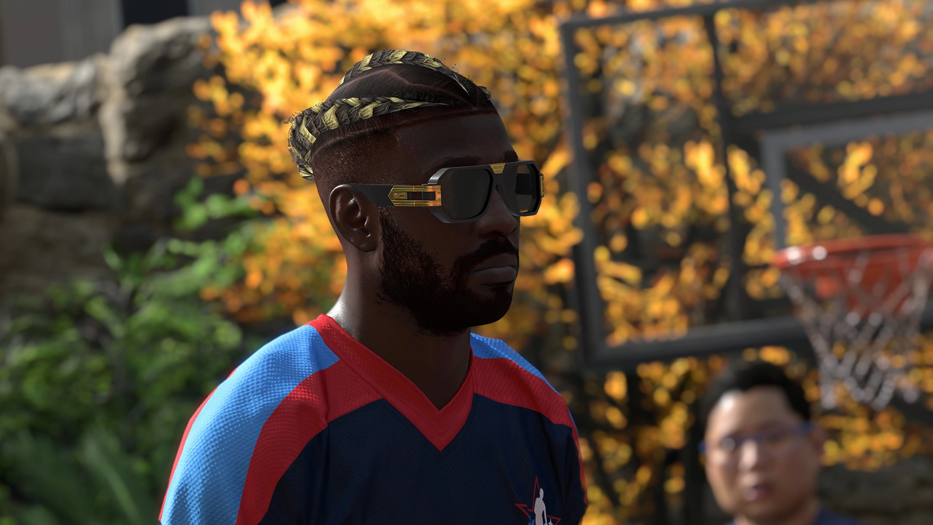 A basketball player wearing sunglasses and a blue jersey stands outdoors with autumn leaves in the background