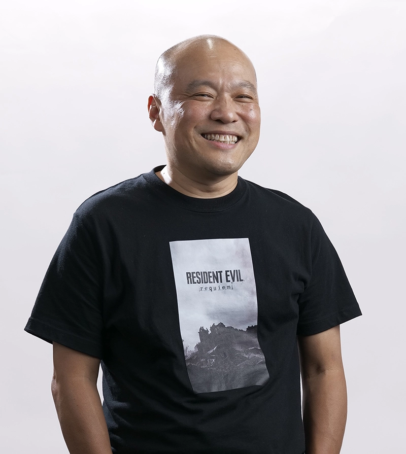A smiling man wearing a Resident Evil Requiem t-shirt, promoting the latest game release
