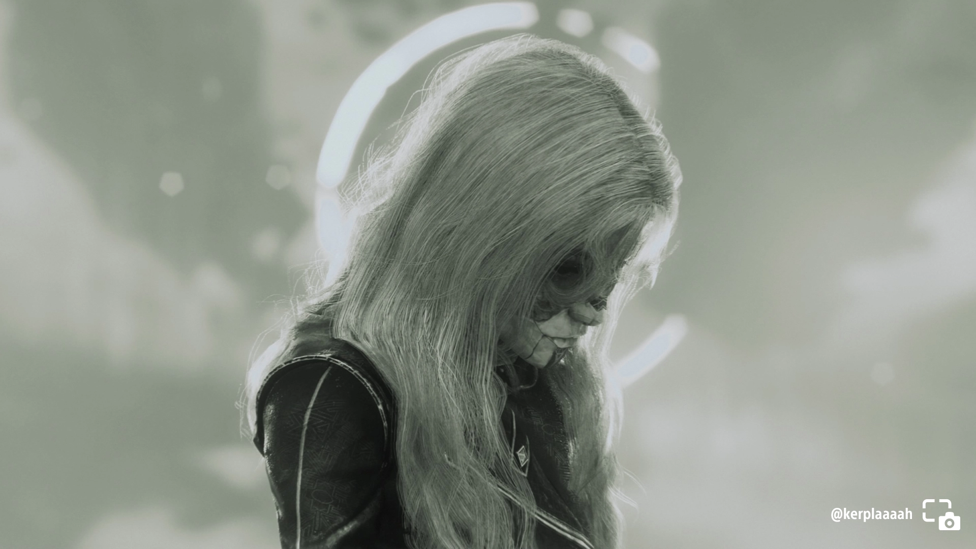 Alicia in black and white, looking downcast, with long hair and a somber expression, background blurred