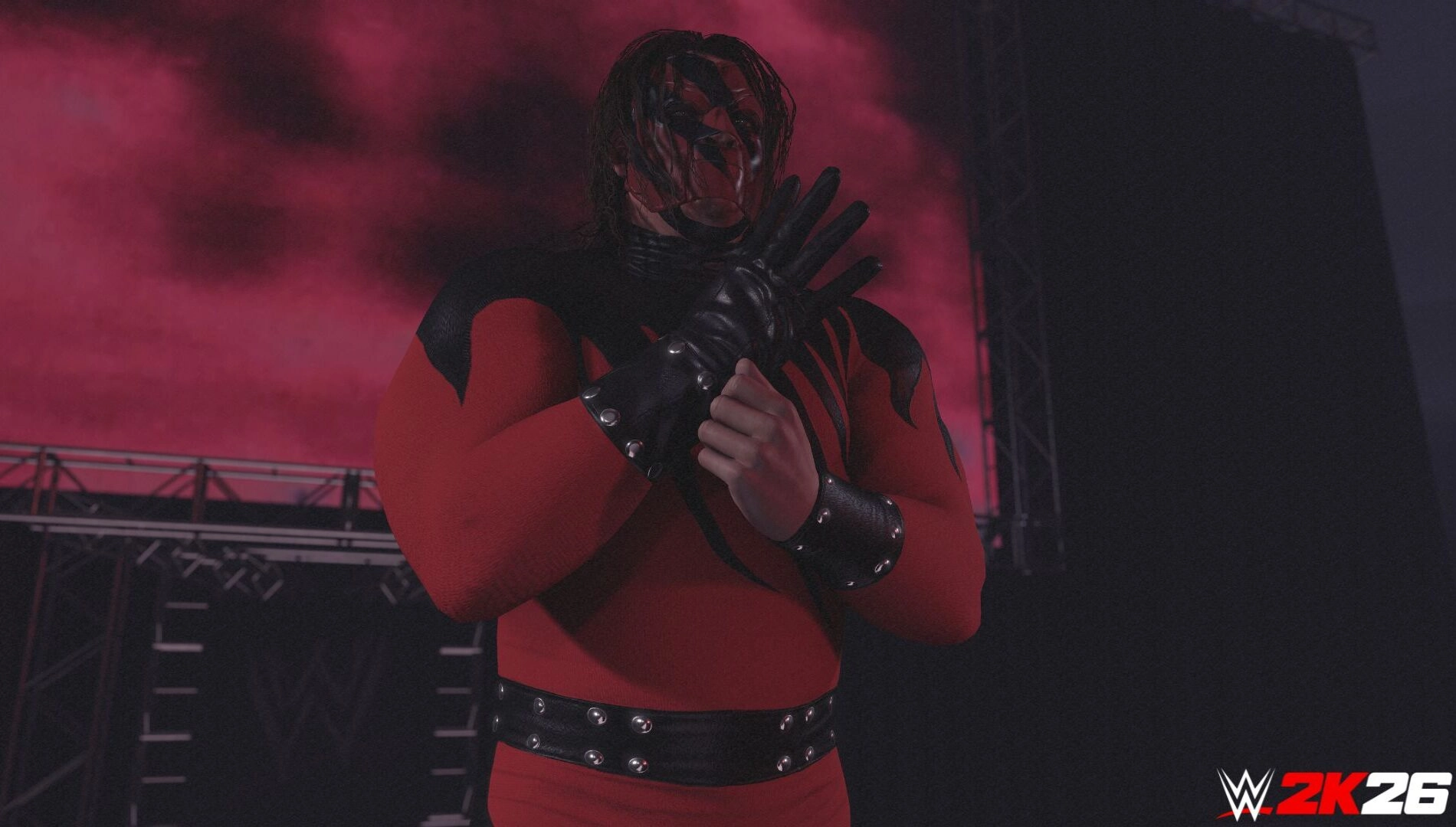 Wrestler in red and black attire stands on stage with red lighting, featured in WWE 2K26 game promo