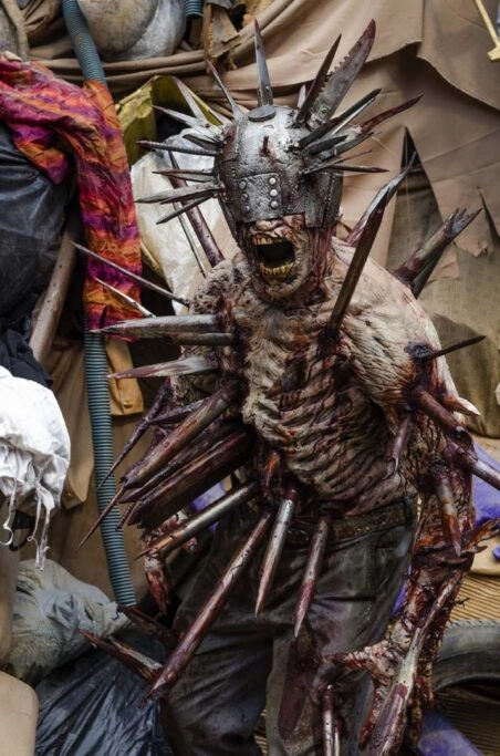 A grotesque zombie with metal spikes and a helmet, set in a chaotic, debris-filled environment