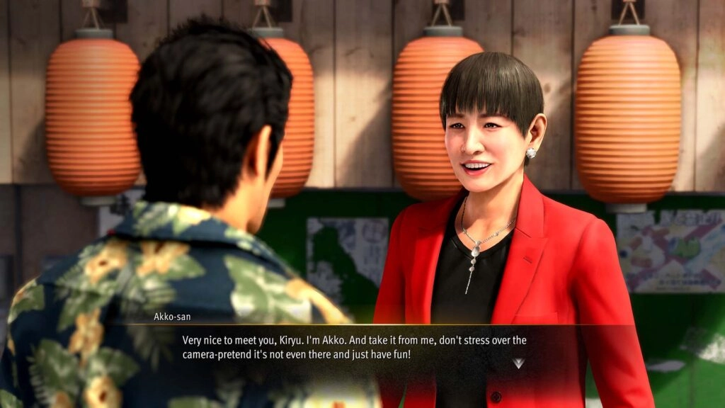 Kiryu converses with a woman in a red jacket, standing in front of traditional Japanese lanterns