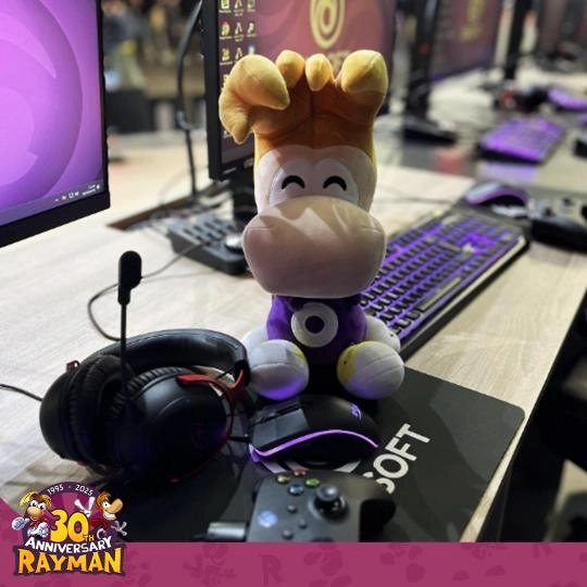 Rayman plush toy sits on a gaming desk with headphones and a controller, celebrating 30 years of Rayman