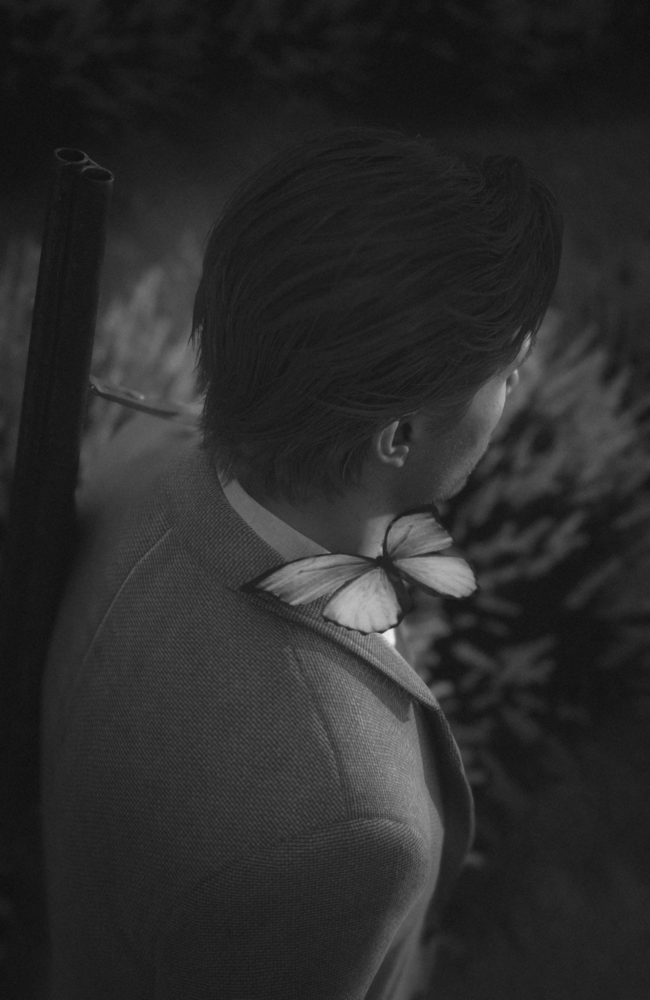 Man in suit with butterfly on shoulder, holding shotgun in serene black and white environment